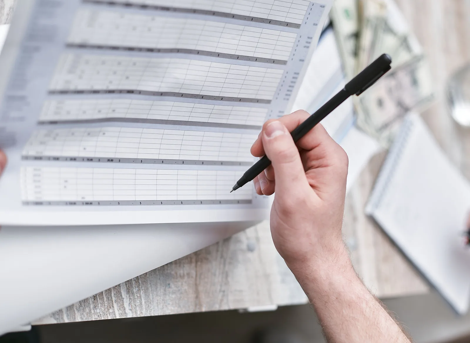 A close-up of a person holding a pen reviewing a financial document with cash visible, ideal for business themes. How to judge a fraud detection tool: the criteria that matter