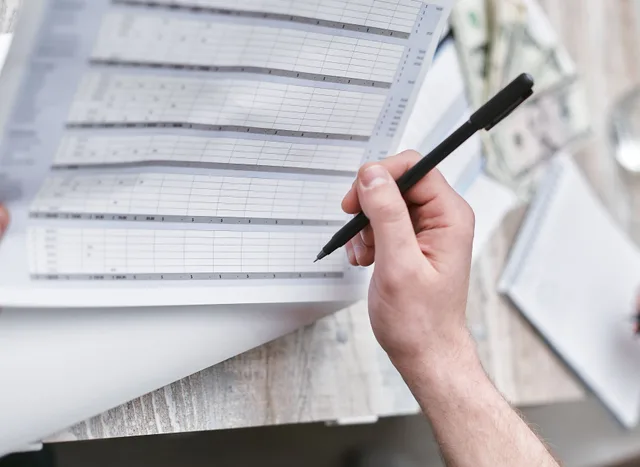 A close-up of a person holding a pen reviewing a financial document with cash visible, ideal for business themes. How to judge a fraud detection tool: the criteria that matter