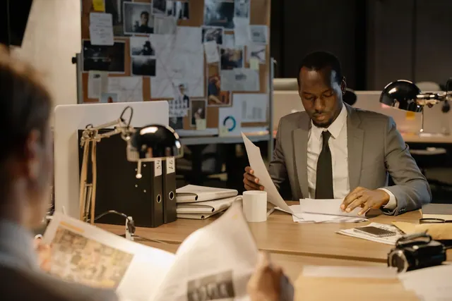 Detective in a suit examines papers at desk in a dimly-lit office, suggesting investigation work. 6 points on choosing fraud detection tools